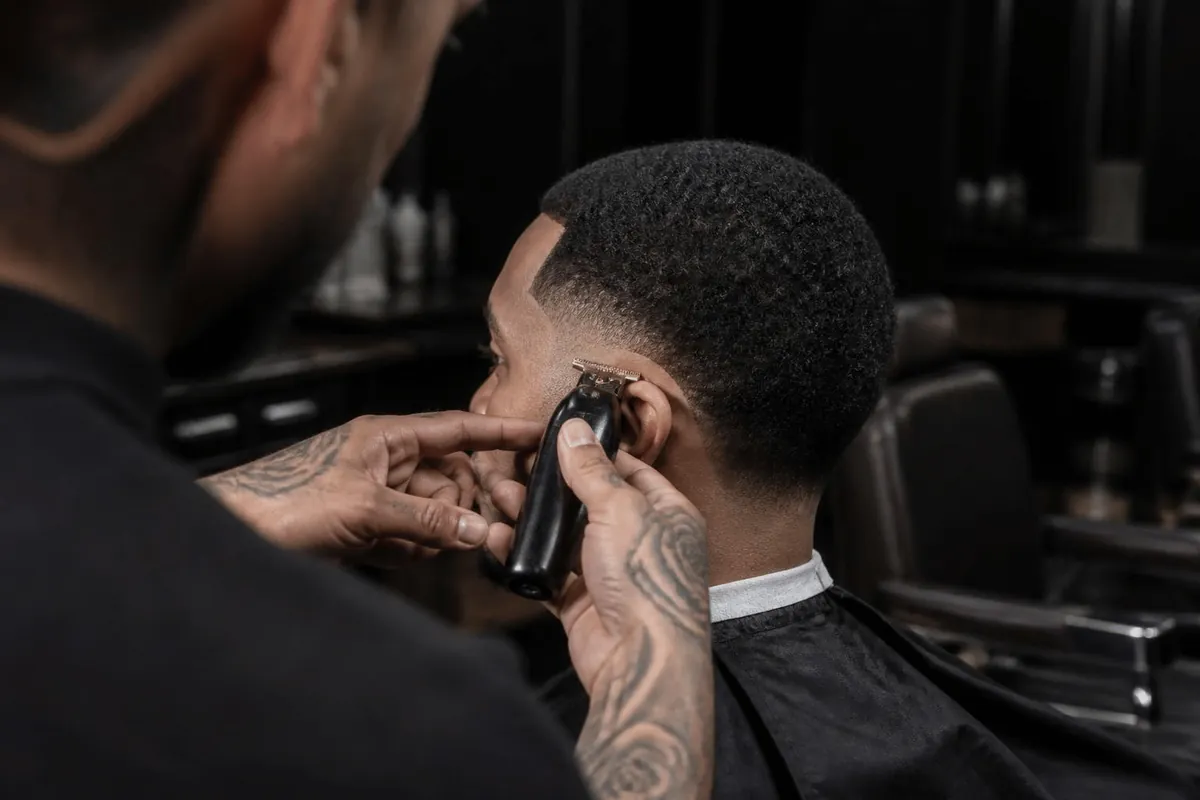 Barber trimming a low taper fade sideburn with a trimmer